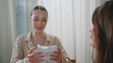 Gülümseyen bayan, yakın plandaki bayan arkadaşına hediye kutusu veriyor. Mutlu esmer kız arkadaşından heyecanlı bir şekilde sürpriz alıyor. Neşeli iki kadın, etkinlikte hediye paylaşımından hoşlanır..