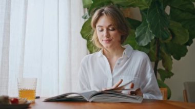 Bayan, daire masasında moda dergisinin keyfini çıkarın. Sabah kahvaltısında gazete okurken sayfaları çeviren sakin bir kadın. Beyaz tişörtlü, düşünceli bir kız. Sakin, sakin bir sabah, günlüğüyle..