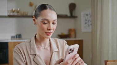 Şık bir iş kadını, iç çekimde cep telefonu bildirimi okuyor. Akıllı telefonlu mutfak masasında e-posta karıştıran zarif bir kadın. Güzel bayan evde cep telefonu ekranına bakıyor..