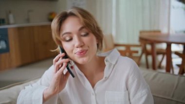 Dinlenen bayan çağrıya cevap veriyor. Rahat koltukta oturuyor. Yakın plan. Oturma odasındaki koltukta cep telefonuyla konuşan gülümseyen kadın. Kaygısız çekici kız evde arkadaşça akıllı telefon konuşmalarının tadını çıkarıyor.