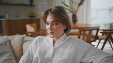 Rahat bayan, beyaz gömleğiyle kanepede oturur ve kendini mutlu hisseder. Huzurlu kadın, sakin bir sabah geçiriyor. Mutlu kız rahat bir evde dinleniyor. Kameraya bakıyor..