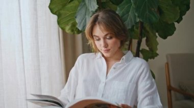 Güzel bayan dergisi yeşil bitkilerle dolu rahat bir dairede oturuyor. Rahat bir kadın, sakin bir sabahın keyfini çıkarıyor. Sayfaları periyodik olarak çeviriyor. Beyaz gömlekli güzel kız hobiyle meşgul..