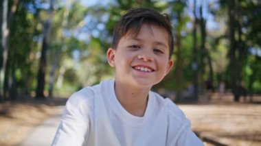 Neşeli çocuk güneş ormanı portresine bakıyor. Mutlu gülümseyen çocuk güneşli yeşillik parkında eğleniyor. Esmer küçük çocuk tatilleri dışarıda geçirmekten hoşlanıyor.