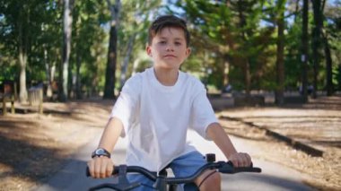 Yaz Ormanı Portresi 'nde bisiklete binen küçük çocuk. Olumlu küçük çocuk kendini kaygısız hissediyor Sunny Park 'ta yakın mesafeden sürüşün keyfini çıkarıyor. Aktif çocuk kameraya bakıyor güneş ışığına doğru eğiliyor doğa zum yapıyor