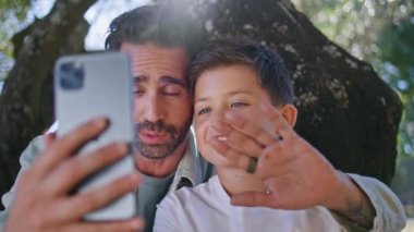 Aile, bahçedeki ağacın altında cep telefonunu arıyor. Akıllı telefon tutan yakışıklı baba-oğul ilişkisi. Kaygısız baba, çocuğuyla selamlaşan elleri videoya çekmekten zevk alıyor. Çocukluk anıları kavramı 