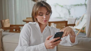 Rahat esmer, akıllı telefonlar ev koltuğu kapanışında online alışverişler yapıyor. Rahat kadın rahat koltukta oturan cep telefonu ekranına bakıyor. Beyaz tişörtlü güzel bayan apartmanda telefonunu karıştırıyor.