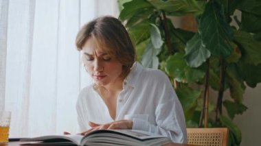 Odaklanmış kadın, dairede portakal suyunu yudumlarken dergi okuyor. Yemek masasında dergi sayfalarına konsantre olan genç ve rahat bir kadın. Güzel kız taze içecekle sabah kahvaltısının tadını çıkarıyor.