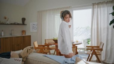 Kablosuz kulaklıklarla müzik dinleyen, modern daireleri toplayan sıradan bir kadın. Tasasız kız sabah rutininde kulaklıkla mutlu bir şekilde dans ediyor. Enerjik bayan ev mutfağında en sevdiği şarkıyı seviyor..