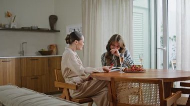 Mutfak masasında birlikte gülen iki kadın. Mutlu güzel bayan arkadaşlar evlerinde neşeli sohbetler ediyorlar. Gülümseyen kızlar, arkadaşça bir toplantıda meyve yiyip sohbet ediyorlar..