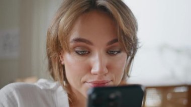 Ciddi bir kadın cep telefonuyla sosyal medyayı izliyor. Oturma odasında rahat rahat oturuyor. Akıllı telefondan romantik masaj okuyan gülümseyen çekici kadının portresi. Mutlu kız çevrimiçi telefon iletişimini seviyor.