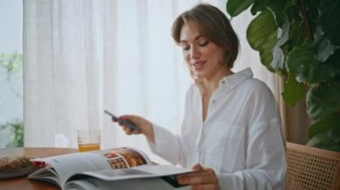 Ev masadaki cep telefonu okuma dergisinde sesli notlar kaydeden mutlu bir kadın. Sabah portakal suyu içen neşeli bayan moda dergileriyle sabahın tadını çıkarıyor. Rahatlamış kız kahvaltı yapıyor..