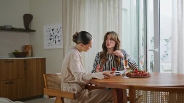 Mutfak masasında konuşan gülümseyen kadınlar moda dergisine benziyor. İki kadın masada içki ve meyvelerle sohbet ediyor. Rahatlamış bayan arkadaşlar evde konuşmanın tadını çıkarıyorlar. Dairede sosyalleşen kızlar