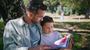 Baba çocuk orman doğasında peri masalı derlemesi okuyor. Sakallı ebeveyn ve çocuk yeşil çimlerde dinleniyor ve kitabın tadını çıkarıyor. Baba oğul, ağaçların altında birbirine bağlanıp parkta sohbet ediyorlar.