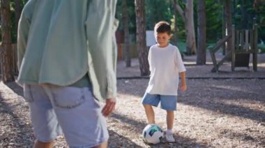 Küçük çocuk güneş parkında futbol oynuyor. Kaygısız çocuk babaya pas veriyor. Birlikte yaz aktivitelerinin keyfini çıkarıyorlar. Aktif bilinmeyen adam küçük çocuk güneş ışığı bahçesinde futbol oynarken eğleniyor.