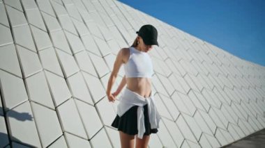 Çağdaş sokak mimarisinin yakınında sıska bir kadın ısınıyor. Kapüşonlu enerjik kadın kollarını uzatarak güneşli caddede sabah antrenmanına hazırlanıyor. Aktif bayan sağlıklı atletizm eğitimi alıyor..