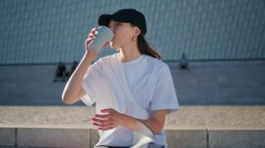 Serene denen kadın sabah güneşinin tadını çıkarıyor. Kapalı alanda. Rahatlamış kız sıcak kahveyi yudumluyor güneşli sokakta sakinliğini hissediyor. Güzel bayan şehir merdivenlerinde yalnız başına dinleniyor..