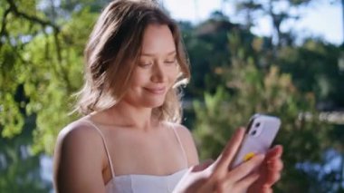 Güneşli rıhtımda cep telefonuyla selfie çeken bir portre kadın. Çekici genç bayan hafta sonu doğa kapanışında yüz resmi yapıyor. Mutlu kadın cep telefonu kamerasına gülümsüyor.
