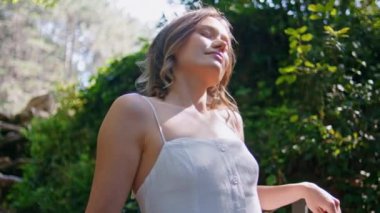 Doğanın tadını çıkaran şefkatli bir bayan. Huzurlu bir ortamda rahatlar. Yakın plan. Sağlıklı odaklı romantik kadın yeşil güneşli park portresindeki huzuru arıyor. Güneş ışığının tadını çıkaran gülümseyen kız