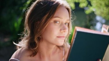 Nazik bir kadın, elinde kitap tutarak güzel, güneşli bir portrede tek başına oturuyor. Romantik bayan Green Park 'ın yakın çekiminde yüzünü romanla kaplayan kameraya bakıyor. Bahçede poz veren flört mankeni. Edebiyat hobisi