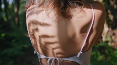 Ormanın yakınındaki eğrelti otu gölgesinde bir kadın. Yeşil vahşi ormanlarda parlak güneş altındaki yumuşak model kız vücudu parlıyor. Tanımlanamayan hassas bayan yemyeşil bitkilerin bahçesinde duruyor güneş ışığını yansıtıyor.