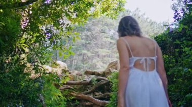 Yeşillik arka manzaralı, ormanlara giden muhteşem bir kız. Güzel yeşil bahçede yürüyen zarif, güler yüzlü bir kadın. Kaygısız kadın, sabahları beyaz elbiseler içinde parkta geziniyor. 