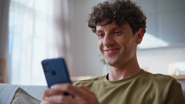 Rahat iş adamı cep telefonuyla mesajlaşıyor. Dairedeki kanepeye yakın oturuyor. Gülümseyen mutlu adam akıllı telefondan mesaj atıyor. Kanepede dinleniyor. İçerideki cep telefonundan sosyal ağları izleyen sakin bir adam. 