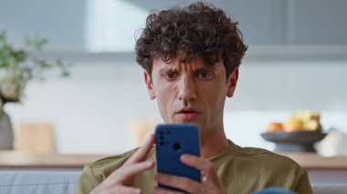 Hüsrana uğramış bir adam aydınlık ev oturma odasında akıllı telefon mesajı okuyor. Memnuniyetsiz adam evdeki koltukta cep telefonuyla mesajlaşırken gergin tepki veriyor. Endişeli iş adamı koltukta cep telefonu ekranı görüyor.