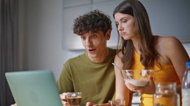 Ev sahibi çift mutfakta kahvaltı yapıyor. Elinde mısır gevreği kasesi olan gülümseyen kadın dizüstü bilgisayarında televizyon programının keyfini çıkarıyor. Aşıklar sağlıklı yemek yerken bilgisayar ekranında video izlerler. 