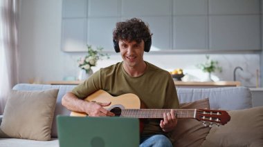 Oturma odasında gitar çalan mutlu bir müzisyen. Gülümseyen adam evde dizüstü bilgisayar kullanarak müzik dersi kaydediyor. Olumlu gitarist dairede telli çalgılar çalarken kafasını hareket ettiriyor. Hobi konsepti 