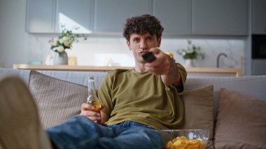 Rahat koltukta tek başına televizyon şovu izleyen sinirli adam. İlginç bir kanal seçen yakışıklı adam uzaktan kumanda düğmesine basıyor. Cidden gevşemiş hipster TV haberleri seyrediyor. Kanepeye yakın oturuyor. 