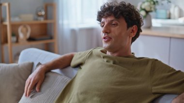 Tembel adamın koltuğa düşüp evinde kendini rahat hissetmesi. Keyfi yerinde gülümseyen kaygısız bir adam. Oturma odasında eğleniyor. Kıvırcık, mutlu, serbest çalışan, dinlenme koltuğu. Rahat bir dairede işe ara veriyor. 