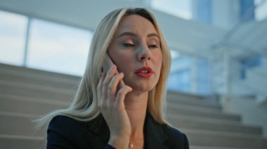 Sarışın menajer cep telefonuyla konuşuyor. İş belgelerini yakından tutuyor. Ciddi bir iş kadını, açık ofis binasında akıllı telefon görüşmesi yaparak sözleşmeyi tartışıyor. Zarif kadın patron anlaşma detaylarını açıklıyor..