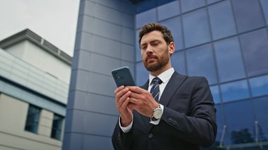 Modern binanın dışında cep telefonundan mesaj okuyan mutlu bir yönetici. Şehir cam bürosunun önünde profesyonel yönetici cep telefonuna mesaj atıyor. Sakallı işadamı dışarıda akıllı telefonu kontrol ediyor..