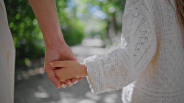 Yeşillikte el ele tutuşan anne çocuğu. Yakın çekim. Tanımlanamayan anne kız parkta yürüyor ve hafta sonları eğleniyor. Anonim bir kadın günü Sunshine Garden sokağında geçiriyor.