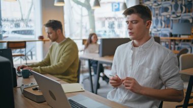 Focused creator typing modern laptop in office interior closeup. Handsome young guy manager looking computer screen writing notes at desk. Serious man comparing work results noticing in notebook  clipart