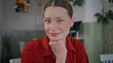 Mutlu kadın rahat kafeteryada kendine güvenen bir şekilde gülümsüyor. Çekici genç bir iş kadınının portresi küçük bir restoranda kameraya bakıyor. Kafe masasında yalnız poz veren kırmızı gömlekli esmer kadın..