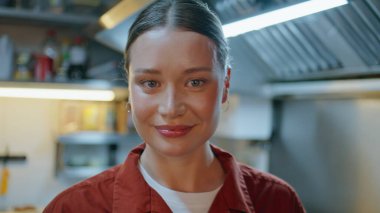 Mutfakta kameraya gülümseyen kadın portresi. Modern restoran mutfağında poz veren genç bir bayan. Mutlu kadın işçiler kafeteryada profesyonel aşçılığın keyfini çıkarıyorlar..