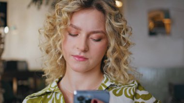 Düşünceli bir bayan cep telefonu ekranında restoranda tek başına oturuyor. Ciddi bir iş kadını iş molasında akıllı telefondan iş mesajı okuyor. İletişim için cep telefonu kullanan çekici bir kadın.