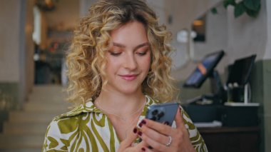 İş kadını cep telefonu sohbetine modern kafede başlıyor. Gülümseyen kıvırcık kadın telefon numarası küçük kafeteryada tek başına oturuyor. Çekici sarışın konuşan cep telefonu kahve dükkanında dinleniyor..