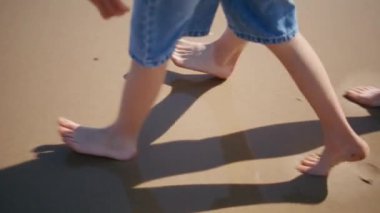 Aile bacakları kaygısız yaz tatilinde kumsalda yürüyor. Çıplak ayaklı anne oğul güneşli tatilde altın deniz kıyısına basıyor. Meçhul bir anne, deniz kıyısında küçük bir çocukla geziniyor.