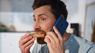 Sabahçı adam akıllı telefondan arıyor ve çikolatalı sandviç yiyor. Orta yaşlı yakışıklı işadamı cep telefonundan konuşup açık mutfakta en sevdiği yemeğin tadını çıkarıyor. Neşeli adam dinleniyor 