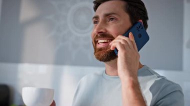 Rahatlamış bir adam akıllı telefonu arıyor ve sabah yakın plan kahve içiyor. Orta yaşlı yakışıklı işadamı cep telefonundan konuşup hafif mutfakta içkinin tadını çıkarıyor. Neşeli adam cep telefonu kullanıyor. 