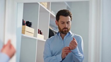 Kendine güveni tam bir yönetici, gömleğinin düğmelerini ilikliyor. Sakallı, ciddi bir iş adamı. Kıyafetlerini giyinme odasında hazırlıyor. Evdeki resmi ayna yansıması.