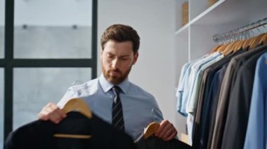 Odaklanmış yönetmen spor ceketi seçiyor ve modern dairede yakın plan çekimde iki şüpheli arasında kalıyor. Sakallı adam ahşap askılar tutuyor ve tek başına büyük gardıroba ayna yansıtıyor. İş hayatı konsepti 