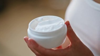 Kadın eli, cilt bakımı sırasında beyaz kavanozdan nemlendirici kozmetik krem alıyor. Meçhul genç bayan anti-yaş kozmetoloji ürünü kullanıyor. Kozmetolojide cilt bakımı organik nemlendirici.
