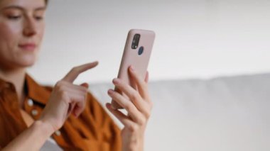 Akıllı telefondan alışveriş yapan, rahat ev kanepesinde rahatlayan gülümseyen bir kadın. Cep telefonlarını dinleyen mutlu bayan internetten alışveriş yapıyor. Daire kanepesinde rahatlamış esmer internette gezinme uygulaması