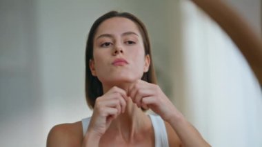 Cilt bakımında boyun masajı yapan kadın aynaya yakından bakıyor. Kırışıklıkları azaltmak için sağIık teknikleri uygulayan nazik bir kadın sağlıklı bir cildi teşvik eder. Çekici esmer masajcı yüz