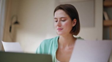 Başarılı bir kadın, yakın plan çekimde dizüstü bilgisayarla ilgili belgeler üzerinde çalışıyor. Bayan finansal analist dairedeki iş evraklarını inceliyor. Gülümseyen serbest çalışan kadın gazete okuyor ve tatmin oluyor.