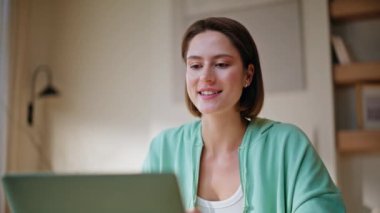 Modern apartmandaki sanal toplantı laptopunda konuşan bir kadın. Gülümseyen esmer kahkahalar evde online video iletişiminin keyfini çıkarıyor. Neşeli serbest çalışanın bilgisayar kamerası kullanarak uzak bir toplantısı var.