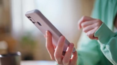 Modern aydınlık dairede cep telefonu tutan kadın elleri. Bilinmeyen bir kız akıllı telefon uygulama dinleme ekranına bakıyor. Cep telefonuyla alışveriş yapan rahat bir bayan..